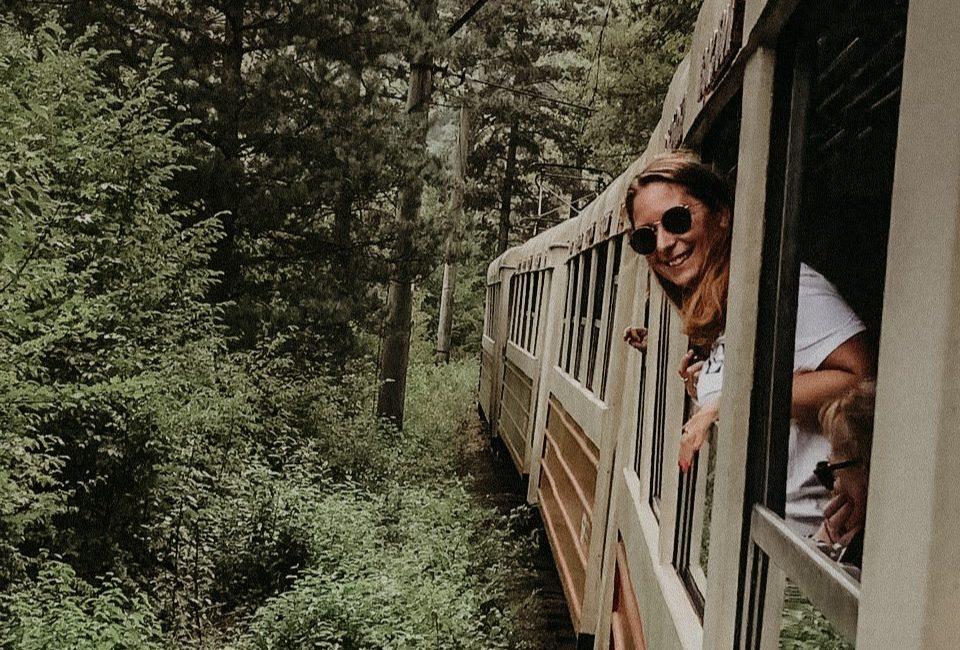 ragazza affacciata dal finestrino di un treno che passa in mezzo alle montagne